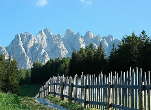 View from the Jora Hut over a wooden fence and green alpine meadow, with striking Dolomite peaks in the background.