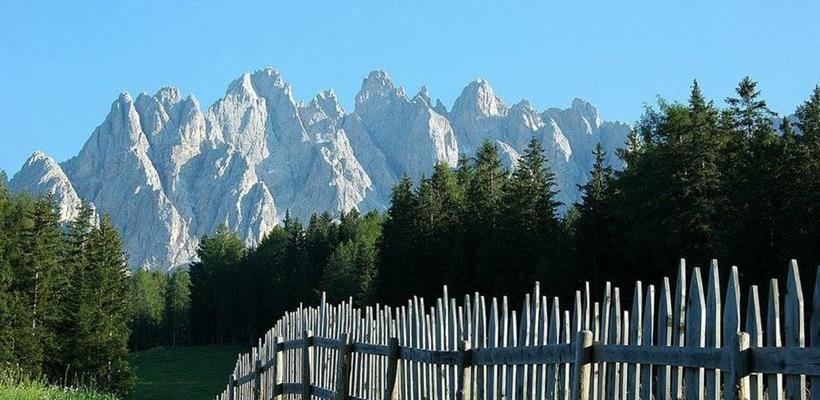 View from the Jora Hut over a wooden fence and green alpine meadow, with striking Dolomite peaks in the background.