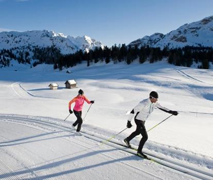 Cross-country skier on a trail in a snow-covered winter landscape, with mountains in the background.