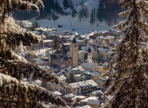 Verschneites Innichen im Winter mit Blick auf den Ort, umgeben von schneebedeckten Bäumen.
