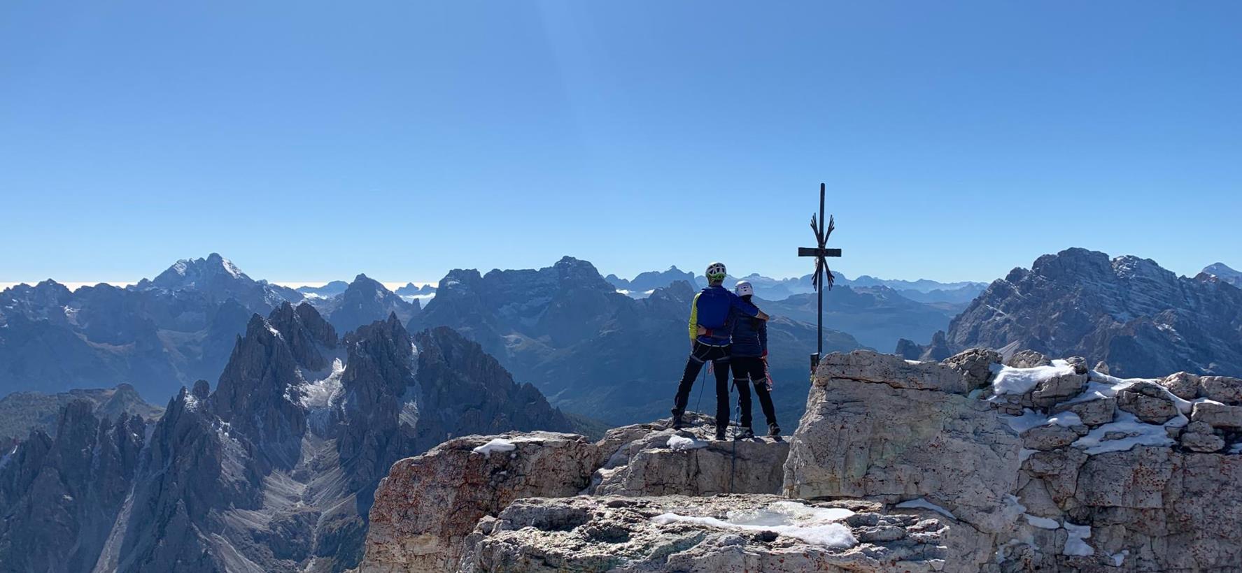 Two climbers stand on a summit and admire the impressive mountain landscape surrounding them.