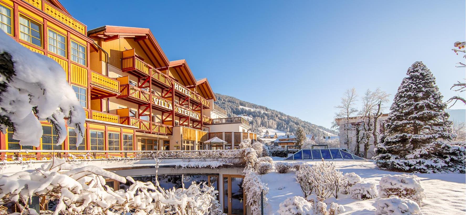 Außenansicht der Villa Stefania in verschneiter Winterlandschaft mit schneebedecktem Garten, Bäumen und blauem Himmel.