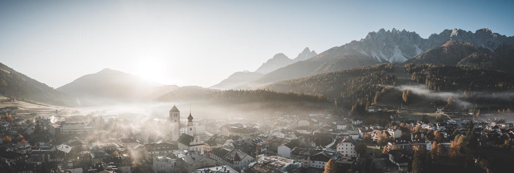 Aerial view of San Candido in autumn with forests and the impressive mountains of the Dolomites in the background.