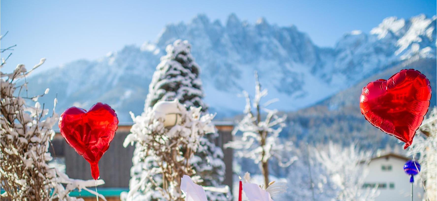 Romantisch gedeckter Tisch mit roten Herzballons im verschneiten Garten der Villa Stefania und Dolomitengipfeln im Hintergrund.