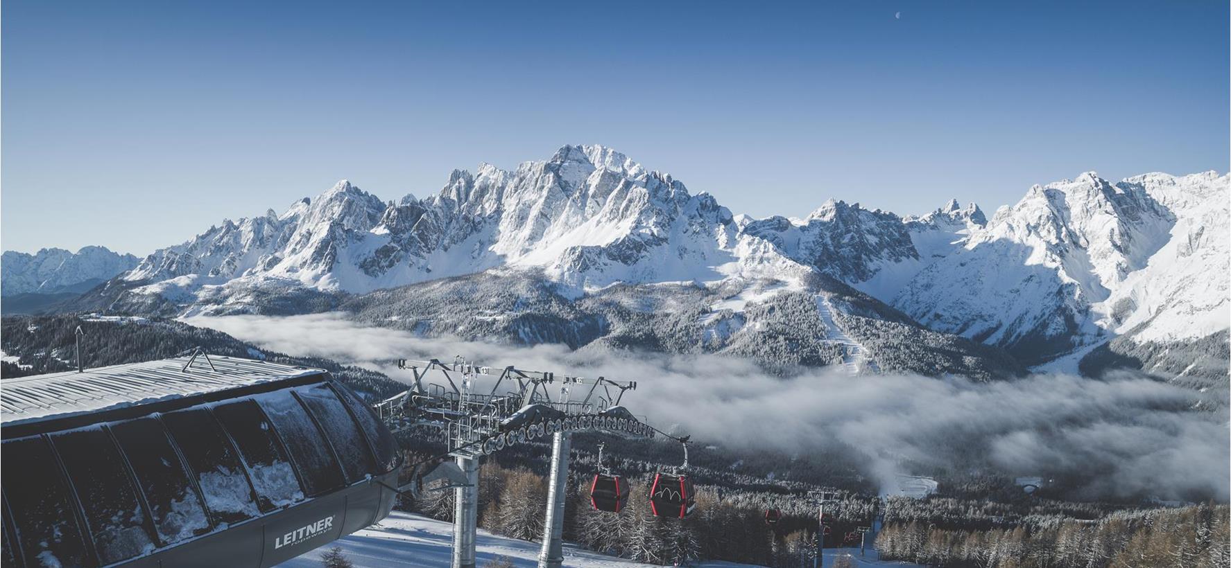 Snow-covered Dolomites with a cable car in front of snow-covered peaks, deep valleys and a winter landscape.