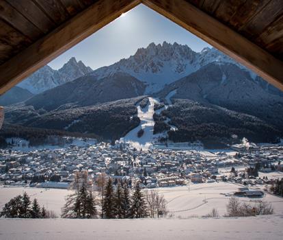 Winter view of San Candido with snow-covered meadows and forests and the striking peaks of the Dolomites in the background.
