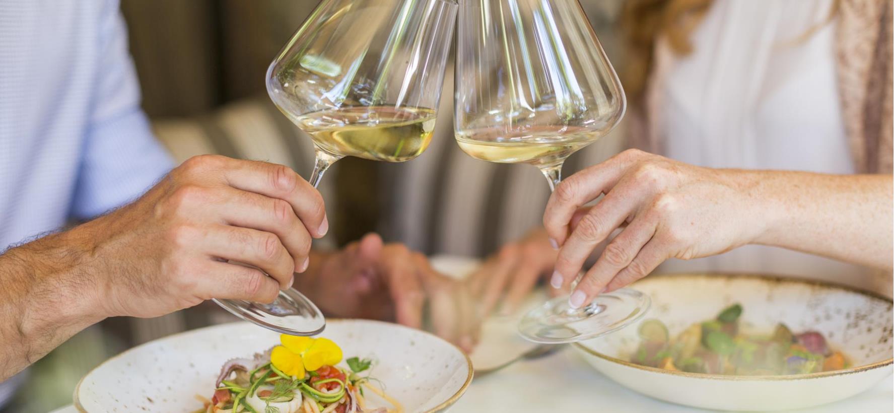 Zwei Personen beim Essen an einem gedeckten Tisch mit Weingläsern im Vordergrund.