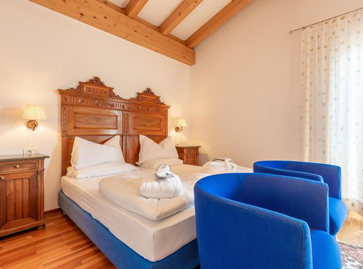 Luminosa Suite Panorama con letto matrimoniale, poltrone blu e travi in legno a vista.