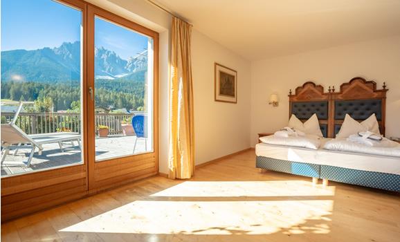 Junior Suite mit Doppelbett und großer Fensterfront mit Blick auf die Berglandschaft der Dolomiten.
