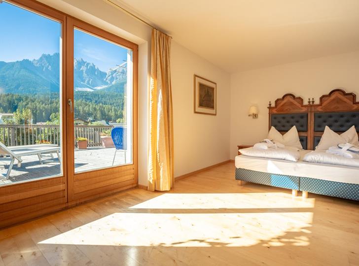 Junior Suite with double bed and large windows overlooking the Dolomite mountain landscape.