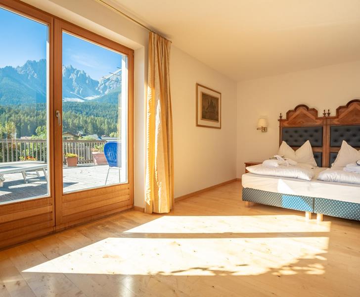 Junior Suite con letto matrimoniale e ampia vetrata con vista sul paesaggio montano delle Dolomiti.
