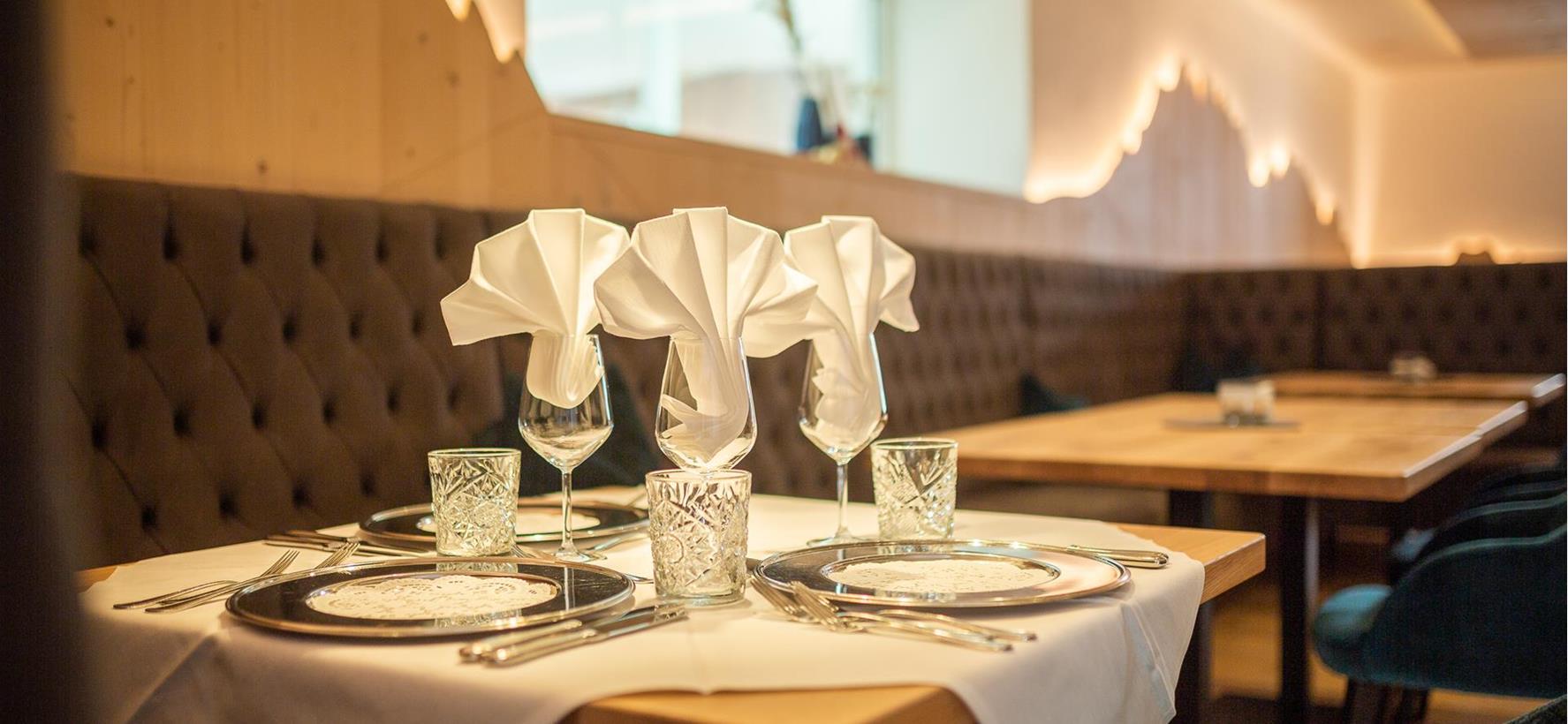 Festively set table in the restaurant at Villa Stefania with white table linen, plates, glasses and folded napkins in front of an upholstered bench.