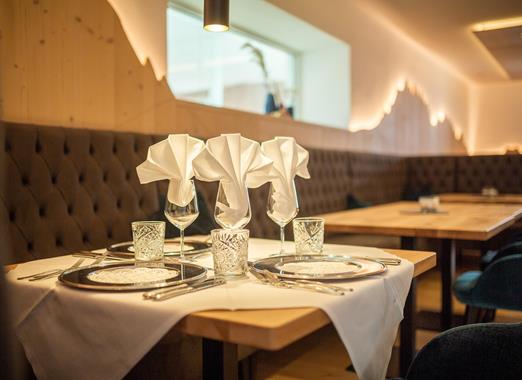Tavolo apparecchiato a festa nel ristorante di Villa Stefania con tovaglia bianca, piatti, bicchieri e tovaglioli piegati davanti a una panca imbottita.