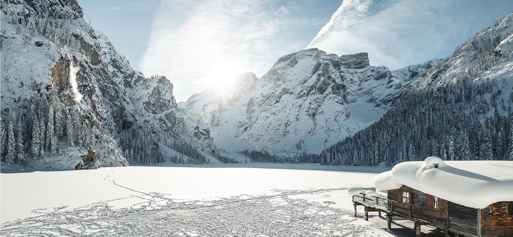 Tief verschneiter Pragser Wildsee im Winter mit Bootshaus und markanten Dolomitengipfeln im Hintergrund.