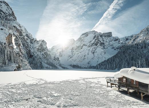 Deeply snow-covered Lake Braies in winter, with a boathouse and the striking peaks of the Dolomites in the background.