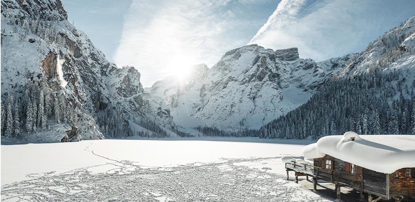 Deeply snow-covered Lake Braies in winter, with a boathouse and the striking peaks of the Dolomites in the background.