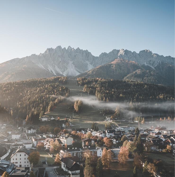 Innichen im Herbst mit herbstlich gefärbten Bäumen und markanten Dolomitengipfeln im Hintergrund.