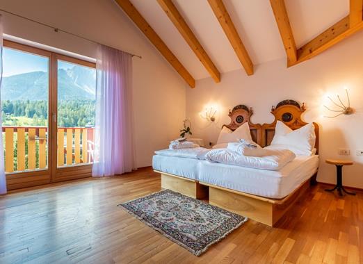 Junior Suite con letto matrimoniale, pavimento in legno chiaro e balcone con vista sulle Dolomiti.