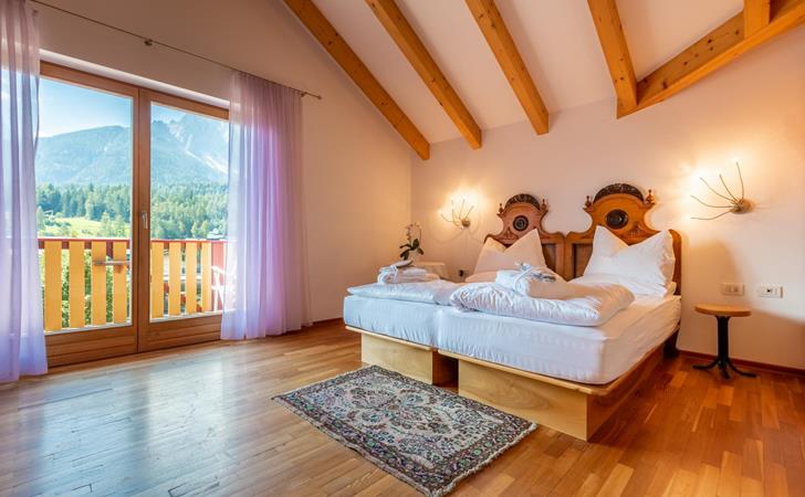 Junior Suite con letto matrimoniale, pavimento in legno chiaro e balcone con vista sulle Dolomiti.
