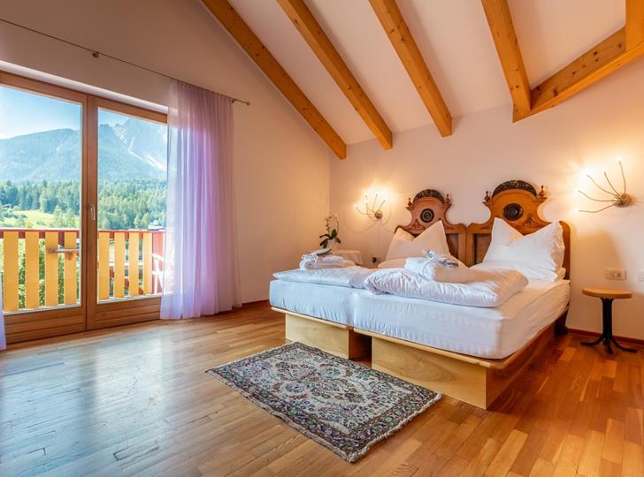 Junior Suite mit Doppelbett, hellem Holzboden und Balkon mit Blick auf die Dolomiten.