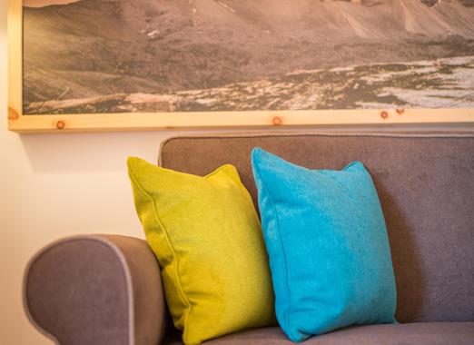 Grey sofa in the Natura Suite with yellow and blue cushions and a picture of the Dolomites above the sofa.