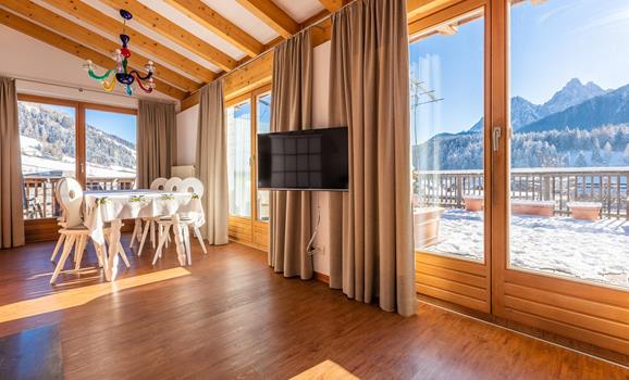 Panorama Suite mit Holzboden, großen Panoramafenstern, gemütlicher Sitzecke und Blick auf die Dolomiten.