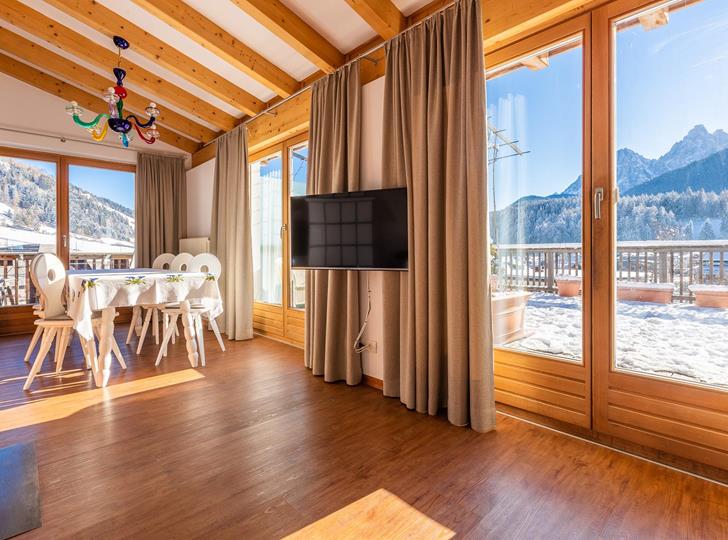 Suite Panorama con pavimento in legno, ampie finestre panoramiche, angolo relax accogliente e vista sulle Dolomiti.