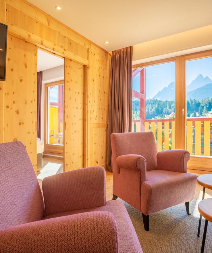 Wohnzimmer der Suite Dolomiti im Hotel Villa Stefania mit gemütlicher Sitzecke, Sesseln, Holzelementen und Blick auf die Dolomiten.