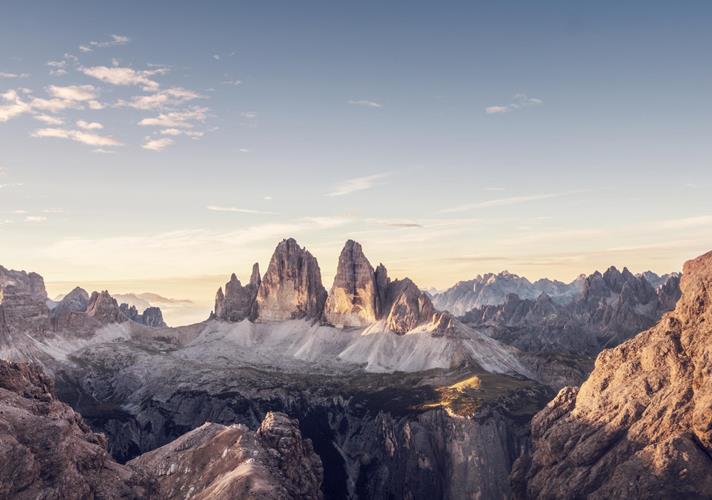 Panoramablick auf die Drei Zinnen in den Dolomiten mit alpiner Landschaft und weichem Licht am Morgenhimmel.