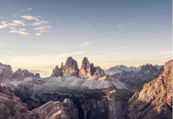 Panoramablick auf die Drei Zinnen in den Dolomiten mit alpiner Landschaft und weichem Licht am Morgenhimmel.