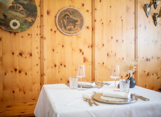 Gedeckter Tisch mit weißer Tischdecke in einer traditionellen Stube mit holzgetäfelten Wänden und dekorativen Tellern.