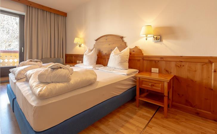 Helles Schlafzimmer mit gemütlichem Doppelbett, Holzmöbeln, warmer Beleuchtung und Blick ins Grüne.