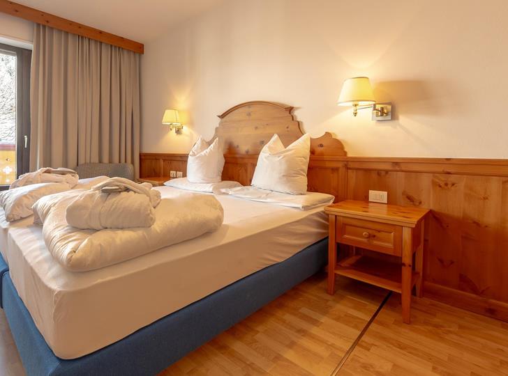 Helles Schlafzimmer mit gemütlichem Doppelbett, Holzmöbeln, warmer Beleuchtung und Blick ins Grüne.
