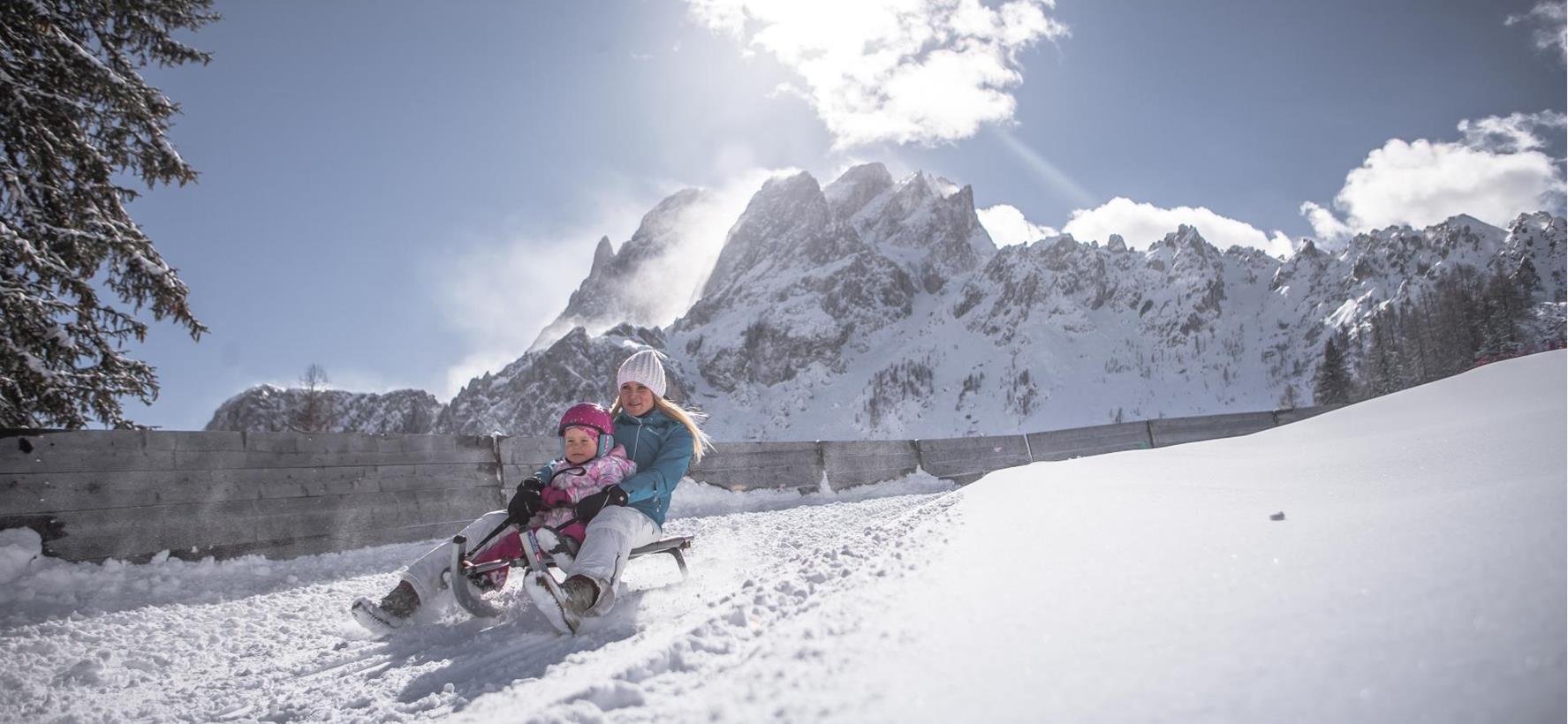 Slittinista in un paesaggio invernale innevato, con imponenti montagne sullo sfondo.