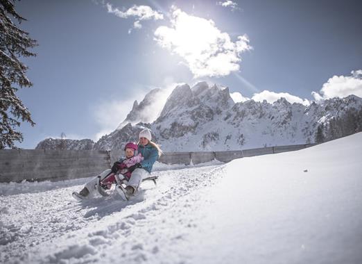 Slittinista in un paesaggio invernale innevato, con imponenti montagne sullo sfondo.