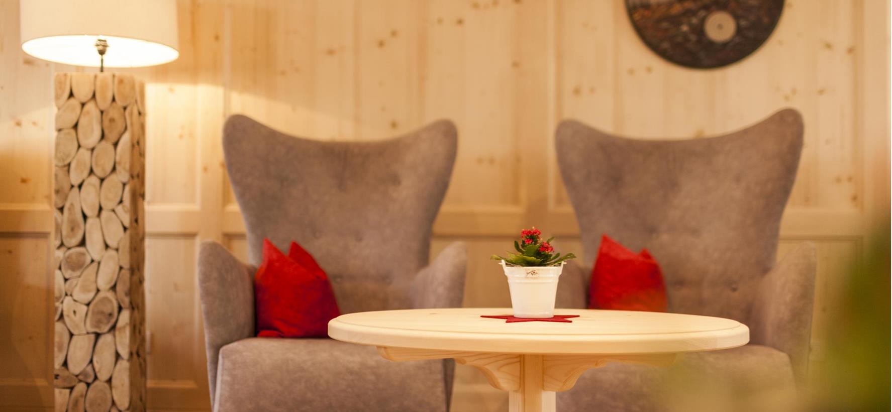 Traditionelle Stube der Villa Stefania mit heller Holzvertäfelung, kleinem runden Tisch und gemütlichen Ohrensesseln.