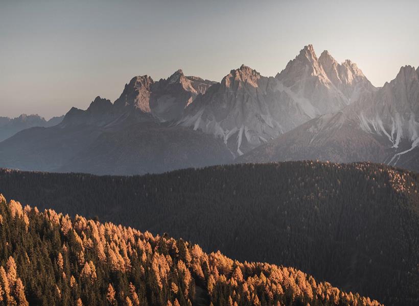 Herbstliche Wälder und das markante Gebirge der Dolomiten im Sonnenschein.