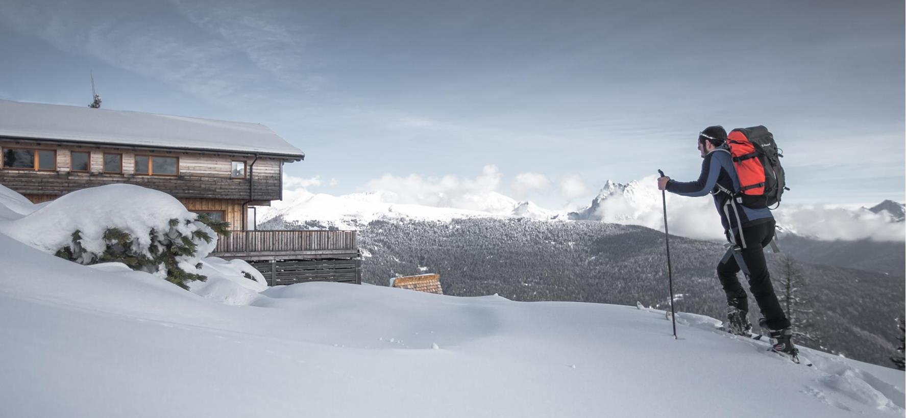 Sci alpinista durante la salita attraverso un paesaggio montano innevato, con cime dolomitiche sullo sfondo.