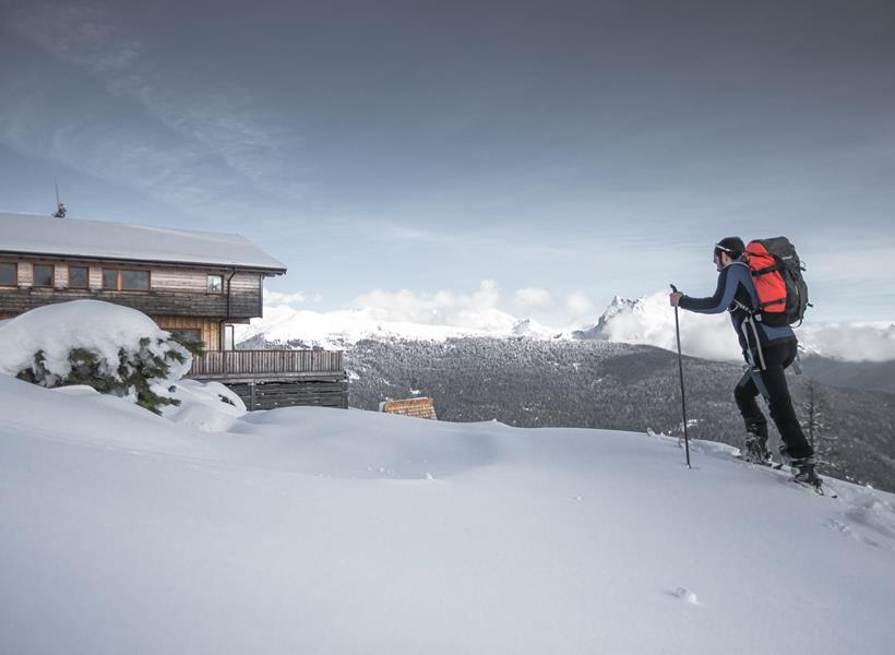 Skitourengeher beim Aufstieg durch eine verschneite Berglandschaft mit Dolomitengipfeln im Hintergrund.