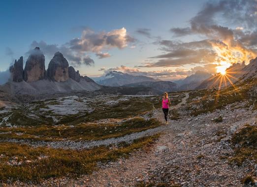 Bergläuferin in steiniger Landschaft im Gebiet der Drei Zinnen bei Sonnenaufgang.