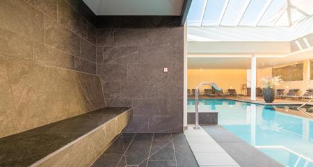 Wellnessbereich mit Sitzbank, Blick auf den Innenpool und Liegestühlen im Hintergrund.