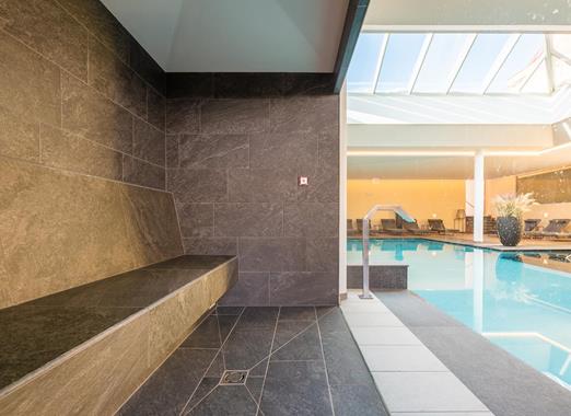 Area wellness con panca, vista sulla piscina coperta e lettini sullo sfondo.