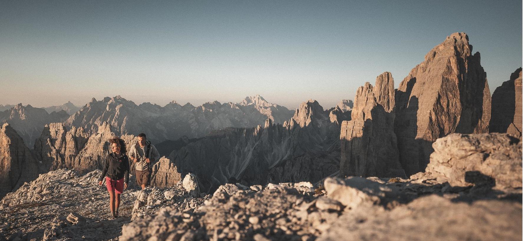 Hikers in a striking landscape with the Tre Cime di Lavaredo and other rock formations in the background.