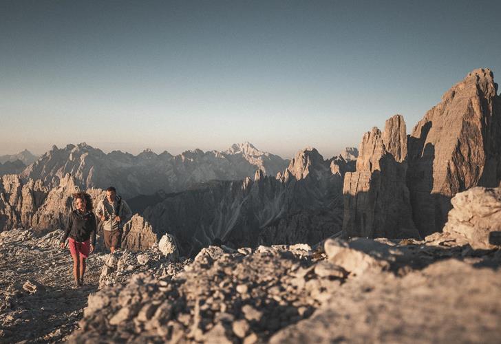 Wanderer in markanter Landschaft mit den Drei Zinnen und weiteren Felsformationen im Hintergrund.