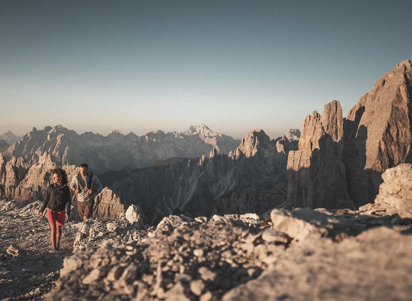 Escursionisti in un paesaggio suggestivo con le Tre Cime di Lavaredo e altre formazioni rocciose sullo sfondo.