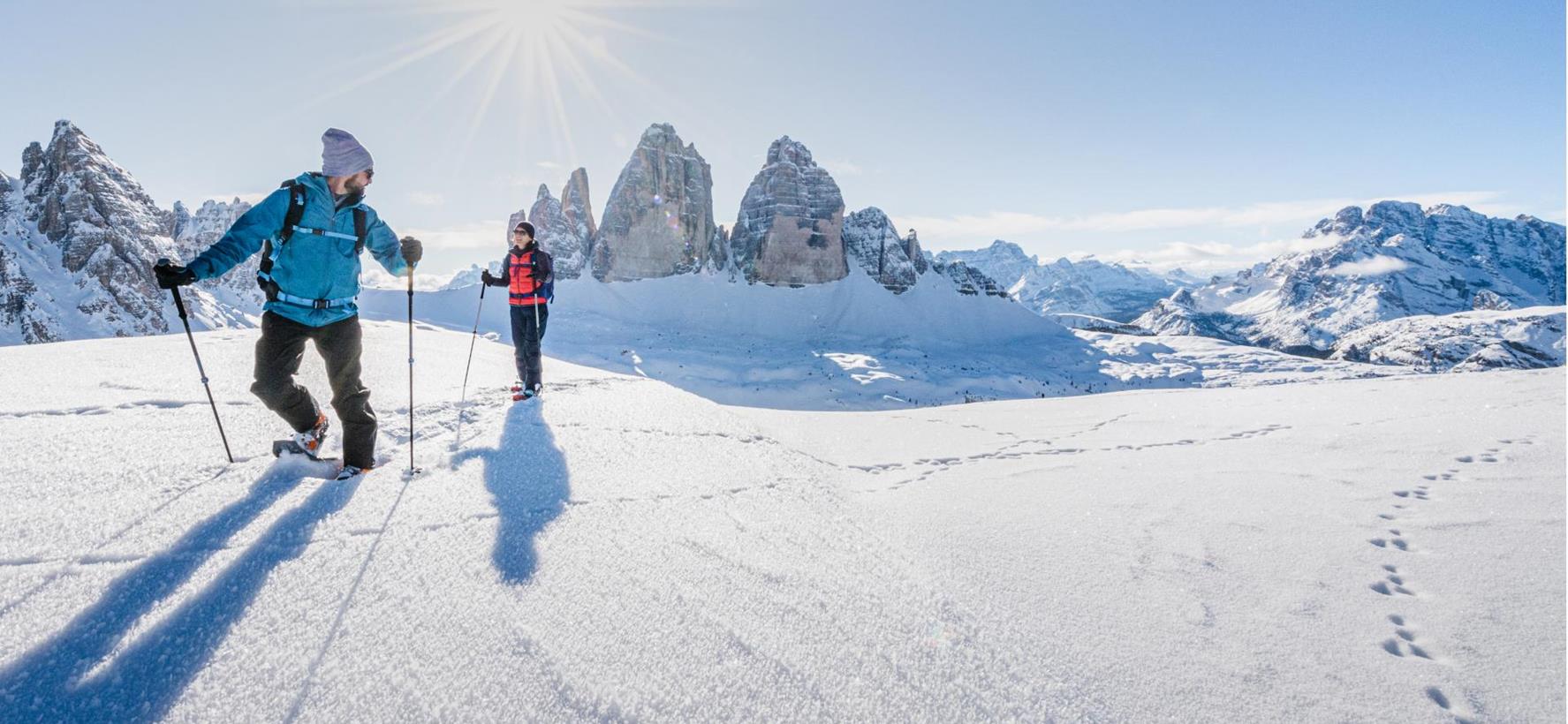 Schneeschuhwanderer in schneebedeckter Landschaft mit den markanten Dolomiten im Hintergrund.