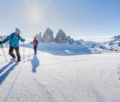 Snowshoe hikers in a snow-covered landscape with the impressive Dolomites in the background.
