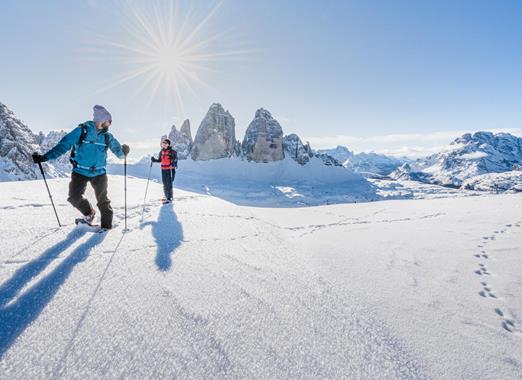 Escursionisti con le ciaspole in un paesaggio innevato con le imponenti Dolomiti sullo sfondo.