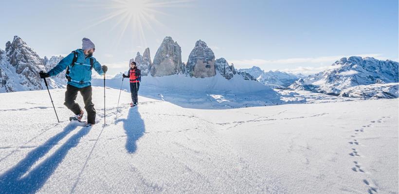 Escursionisti con le ciaspole in un paesaggio innevato con le imponenti Dolomiti sullo sfondo.
