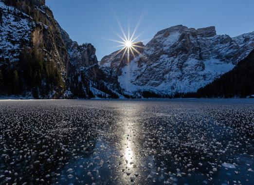 Close-up of the frozen Lake Braies with snow-covered mountains and the rising sun in the background.
